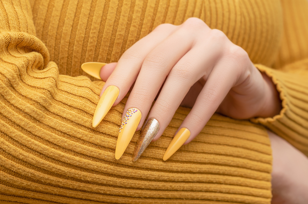 Female hand with yellow nail design. Long nail polish manicure. Woman manicure with gitter gold long nail art.