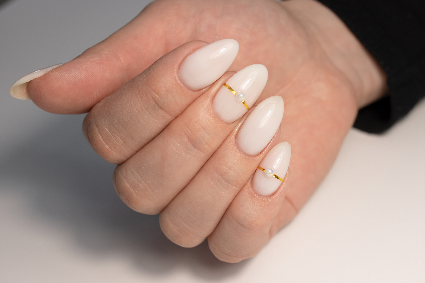 Beautiful nude manicure with pearls and gold stripes. Manicure for women with gel polish. Long nails in the shape of almonds